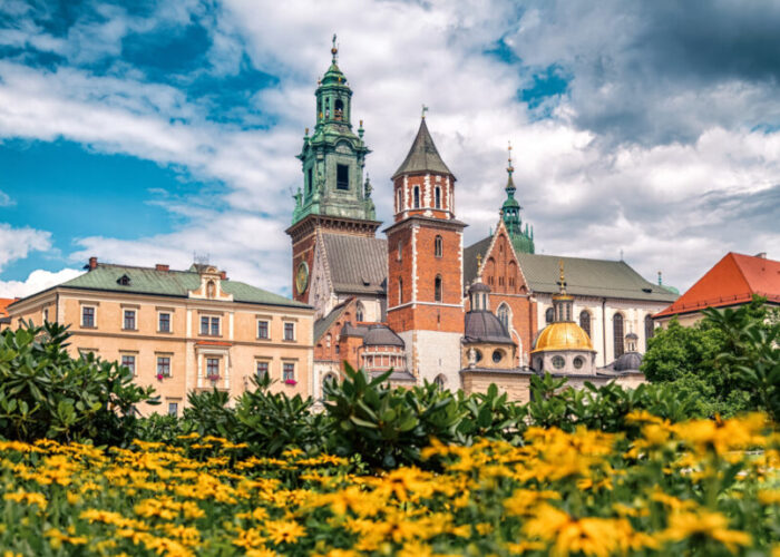 Wawel Royal Castle and Cathedral in Krakow, Poland seen from garden with yellow flowers under blue sky